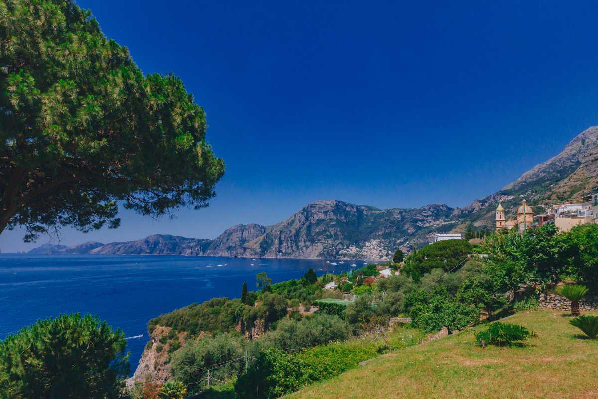 Scatto ampio di una famiglia con bambini piccoli che si gode una passeggiata nei giardini di Villa Rufolo, con Ravello sullo sfondo e giochi d'acqua in primo piano
